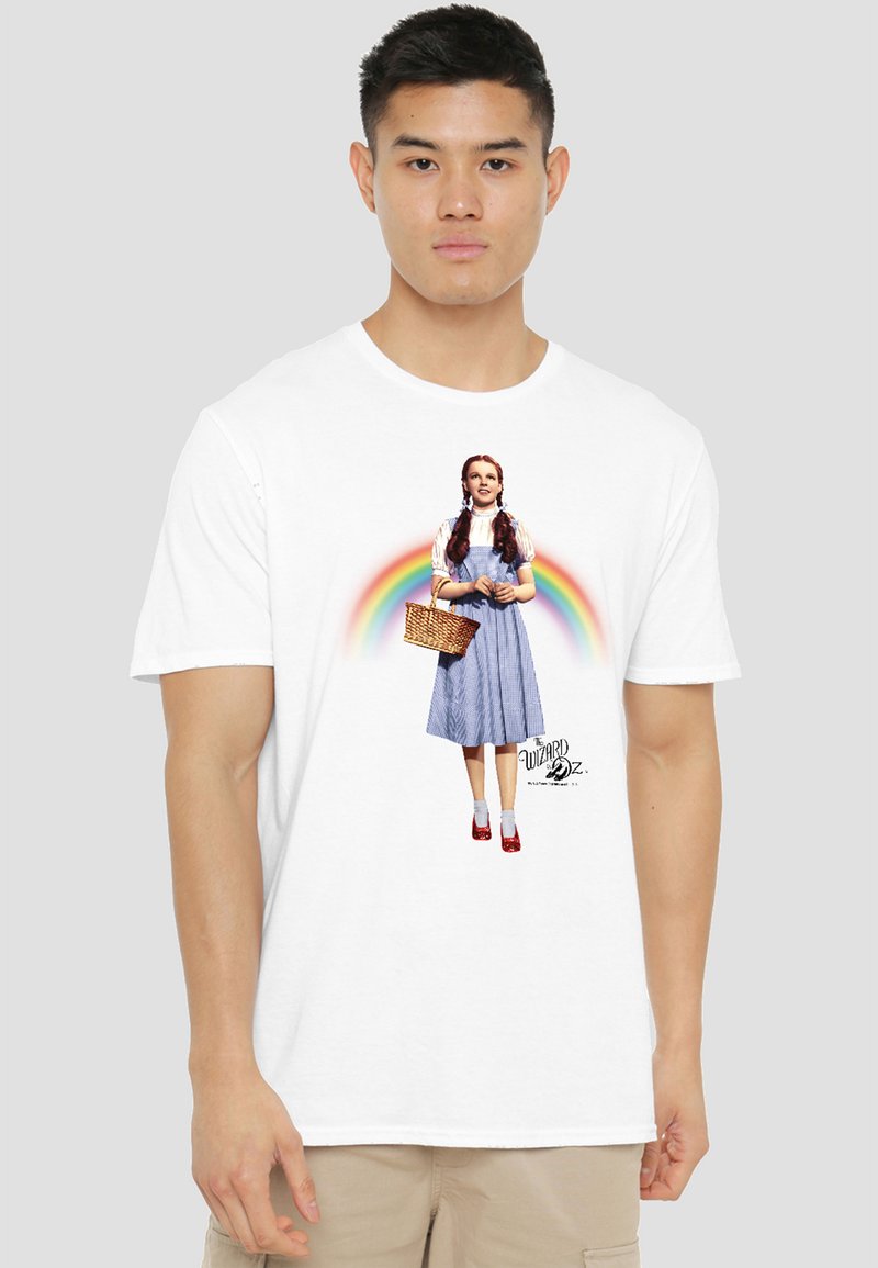 Young man wearing white t-shirt featuring Dorothy from The Wizard of Oz with a rainbow behind her and a basket in her hand.