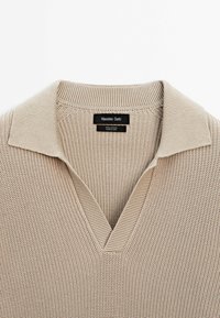 Pull en tricot beige avec un col en V côtelé et un col court, étiqueté Massimo Dutti, 100 % coton, fabriqué en Chine.