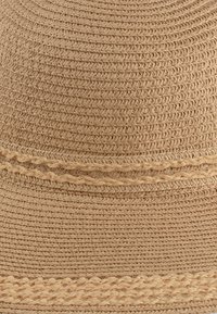 Jasnobrązowy kapelusz słomkowy o tkanej teksturze, z plecioną opaską wokół korony i szerokim, zaokrąglonym rondem.