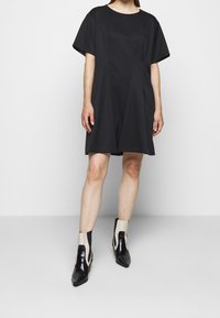 Vestido negro de manga corta con escote redondeado y detalles de costura geométrica. Combinado con botas hasta el tobillo en negro y crema con diseño recortado.