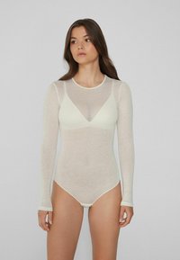 Bodysuit s dlouhým rukávem z průhledné bílé látky, s kulatým výstřihem a V-čelním designem. Obsahuje patentky na dně.