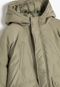Olijfgroene pufferjack met een capuchon, met zijzakken, een rits aan de voorkant en gestikte details op een glanzend, textured oppervlak.