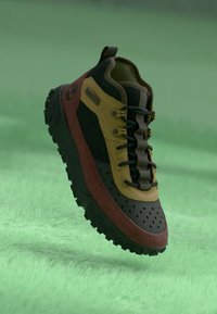 Trail tenisice koje se sastoje od kombinacije smeđe, crne i žute boje, s teksturiranim gornjim dijelom, mrežastim panelima i čvrstim potplatima.