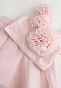 Vestido rosa con corsé ajustado adornado con tres grandes flores de tela suave. Falda transparente con capas, textura sutil y botones decorativos dorados.