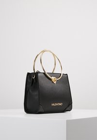 Svart läderhandväska med en strukturerad design, gyllene cirkelhandtag och ett hjärtformat accent. "VALENTINO"-logotypen syns på framsidan.