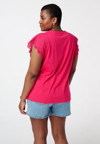 Felroze katoenen t-shirt met geschulpte gehaakte mouwtjes, gecombineerd met lichte denim shorts. Soepele textuur, casual ontwerp.