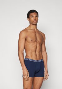 Boxers navy avec une taille blanche marquée. Le tissu semble doux et ajusté, mettant en valeur la forme et la texture du corps.