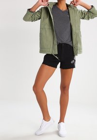 Grøn letvægtsjakke med to forlommer, båret over en grå T-shirt. Sammen med sorte denimshorts og hvide sneakers.