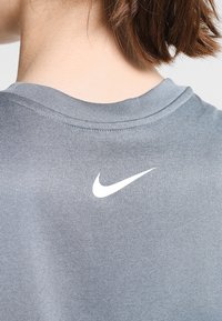 Grijze Nike t-shirt met een ronde hals en korte mouwen, voorzien van een witte swoosh-logo nabij de achterkant van de hals. Glad aanvoelend.