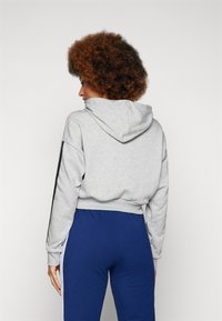 Grijze cropped hoodie met een trekkoordcapuchon, voorzien van zwarte zijstrepen, gecombineerd met blauwe broeken. Soepele textuur, casual ontwerp.