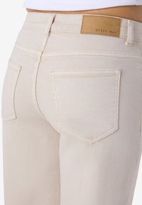 Μπεζ τζιν ψηλόμεσο με πίσω τσέπες και δερμάτινο ετικέτα της μάρκας με την επιγραφή "NOISY MAY" στη ζώνη μέσης.