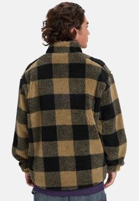 Fleece jacket with a black and beige plaid pattern, featuring a high collar and oversized fit, soft texture, and long sleeves.
