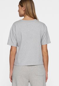 Camiseta gris cortada hecha de una suave mezcla de algodón. Presenta mangas cortas y un sencillo escote redondo, mostrando un ajuste relajado.