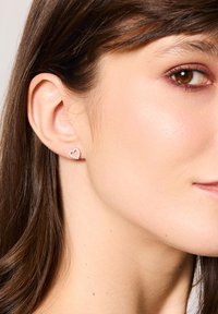 Kolczyki w kształcie serca z różowego złota z małą, teksturowaną, kwiatową ramką. Ozdobione drobnymi, przezroczystymi kamieniami szlachetnymi dla dodatkowego blasku.