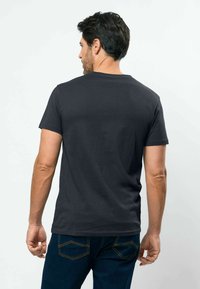 Tamsiai pilka medvilninė marškinėliai su apvalia iškirpte, trumpomis rankovėmis ir lygiu audiniu. Dėvimi su mėlynais džinsais.