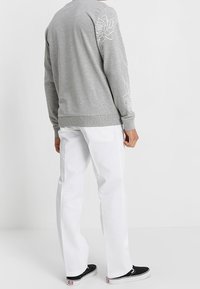 Felpa grigia con ricamo floreale sulla manica sinistra, abbinata a pantaloni bianchi e scarpe slip-on nere. Tessuto testurizzato, vestibilità rilassata.