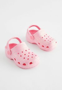Rosa Kunststoffclogs mit glänzender Oberfläche und Glitzer, Belüftungsöffnungen und einem Riemen hinten für sicheren Halt. Abgerundete Zehenpartie und strukturierte Sohle.
