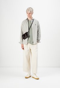 Stribet skjorte i lys grøn og hvid, parret med en grå sweatshirt. Bred beige bukser og beige sneakers. Lille sort crossbody taske.