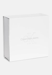 Baltas stačiakampis dėžutė su blizgiais paviršiais, puošta iškilmingu „Calvin Klein Jeans“ logotipu minimalistiniame dizaino stiliuje.