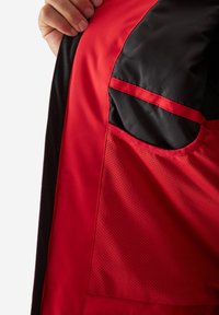 Giacca rossa con un mix di texture lisce e a rete. Accenti neri e un dettaglio tasca sul lato migliorano il suo design funzionale.