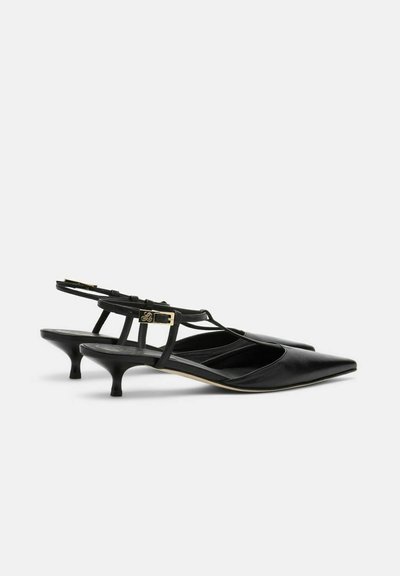 Escarpins à talons bas en cuir noir avec brides arrière, bouts pointus et boucles dorées, vus de profil sur fond blanc.