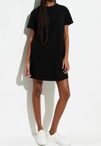 Abito t-shirt in cotone nero con maniche corte e scollo rotondo, caratterizzato da una vestibilità comoda e orlo dritto. Indossato con sneakers bianche.