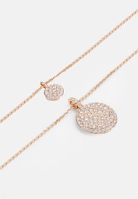 Náhrdelník z ružového zlata so zaobleným príveskom a menším šarmom, oba zdobené trblietavými čírymi rhinestones na jemnom reťazci.