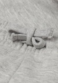 Hellgrauer Baumwollstoff mit einer strukturierten Oberfläche, mit einem gewebten Zugband, das als Schleife am Bund gebunden ist. Flache und glatte Textur.