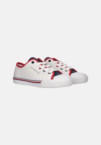 Zapatillas de lona blancas con detalles en rojo y azul marino, punta redonda, cordones blancos y suela de goma con patrón de agarre texturizado.