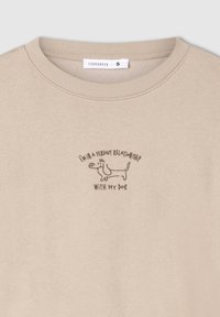 Beżowy sweter z okrągłym dekoltem, z brązowym haftem przedstawiającym psa oraz napisem: "JESTEM W POWAŻNYM ZWIĄZKU Z MOIM PSEM."