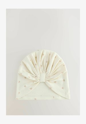 Cappellino per bambino in tessuto crema con piccola stampa floreale rosa e dettaglio a fiocco arricciato sul davanti, su uno sfondo semplice.