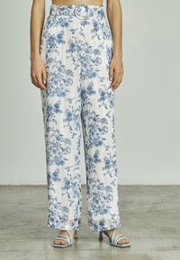 Blumendruck-Hosen mit weitem Bein zeigen einen weißen Hintergrund mit blauen Blumen, einem geknoteten Taillen-Detail und einem leichten, strukturierten Stoff.