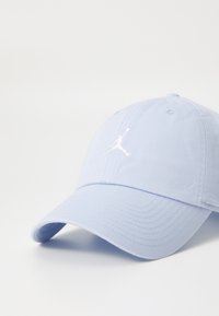 Šviesiai mėlyna medvilninė beisbolo kepuraitė su lenktu kraštu ir baltu išsiuvinėtu Jumpman logotipu priekyje. Yra tekstūruotas audinys ir siuvimo detalės.