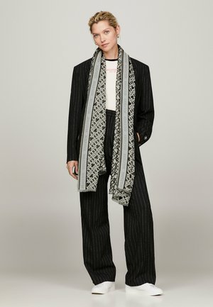Completo a righe nere con top bianco, avvolto in una sciarpa grigia e nera decorata. Presenta pantaloni dritti e sneakers bianche.