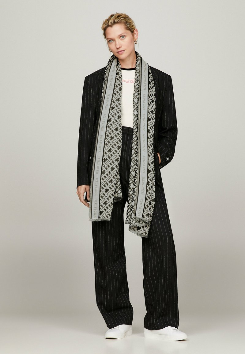 Completo a righe nere con top bianco, avvolto in una sciarpa grigia e nera decorata. Presenta pantaloni dritti e sneakers bianche.