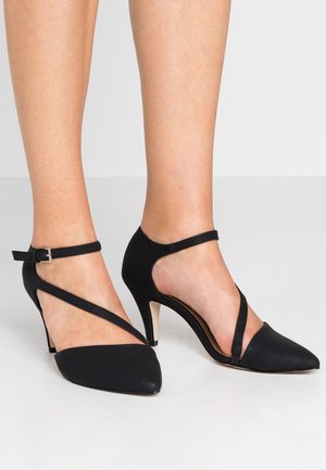 Czarne szpilki z spiczastym noskiem, paskiem na kostkę i krzyżującym się wzorem. Gładki materiał i umiarowany obcas dodają elegancji.