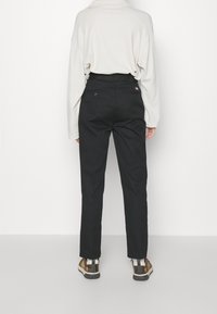 Pantalons noirs à coupe droite, dotés de deux poches arrière, fabriqués dans un tissu lisse. Portés avec un haut beige à manches longues et des chaussures à motifs.