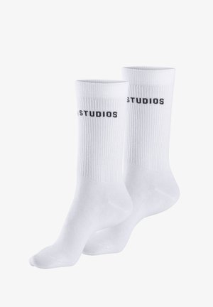 White cotton socks with ribbed texture, featuring black "STUDIOS" branding along the sides, in crew length design.