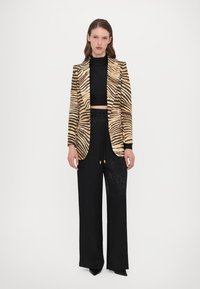 Blazer met een goud en zwart zebrapatroon, twee knopen, gecombineerd met zwarte wijde broek met een subtiele textuur.