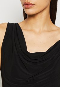 Svart ärmlös topp med draperad båtringning, slät textur och figurnära silhuett som framhäver nyckelben och axlar.
