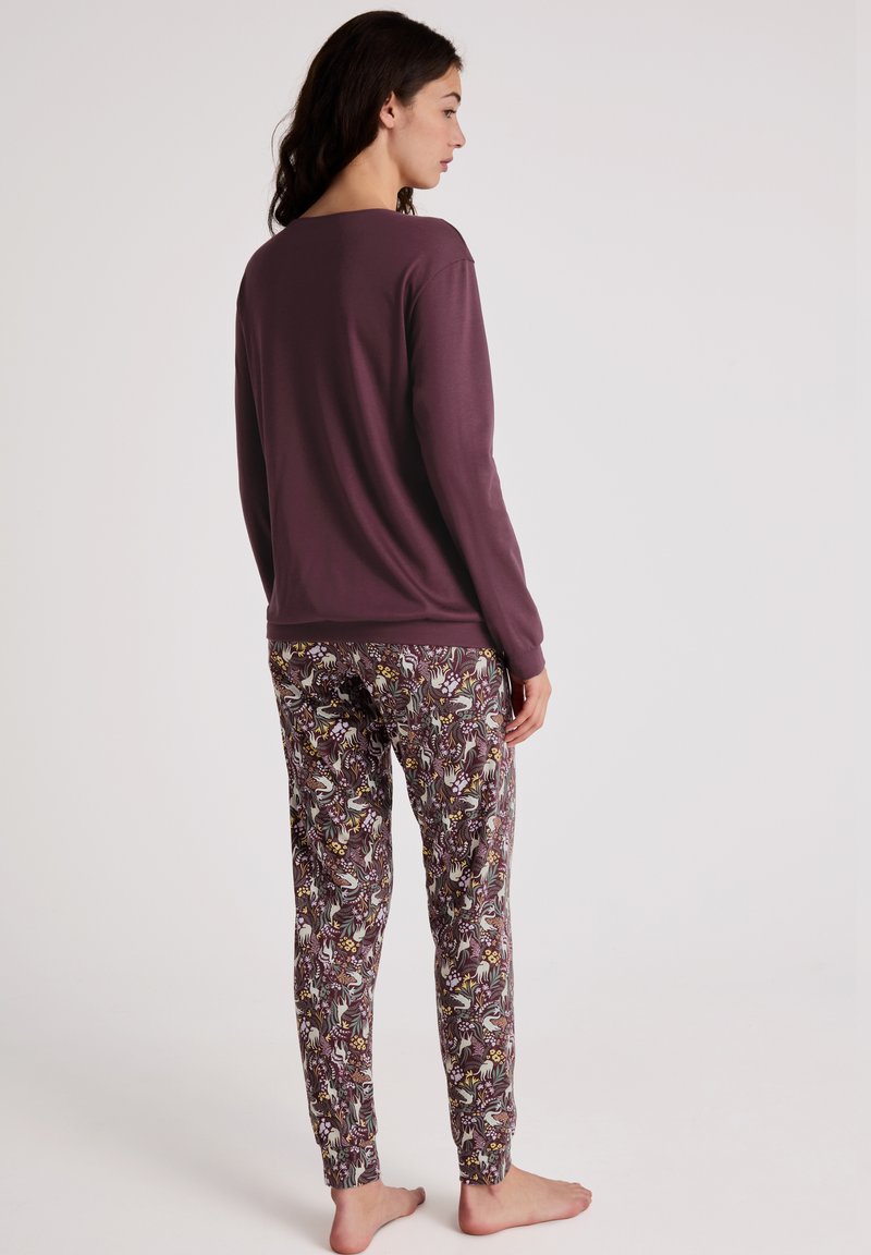 Langsleeve paarse top gecombineerd met gestreepte pyjamabroek met bloem- en dierenontwerpen in gedempte kleuren. Model staat blootsvoets en staat zijwaarts.