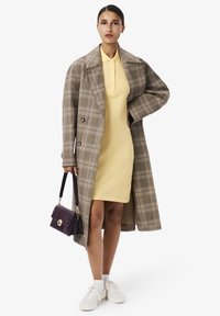 Manteau oversize à carreaux marron, robe polo jaune, baskets blanches et un sac à main violet avec quincaillerie dorée ; textures lisses et formes structurées.