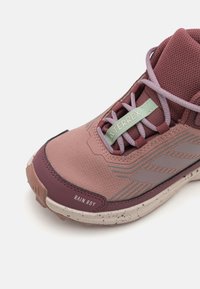 Helle rosa Sportschuh mit strukturiertem Obermaterial, grauen Akzenten und einer Gummisohle. Zu den Merkmalen gehören ein Schnürdesign und das Etikett "RAIN.RDY".