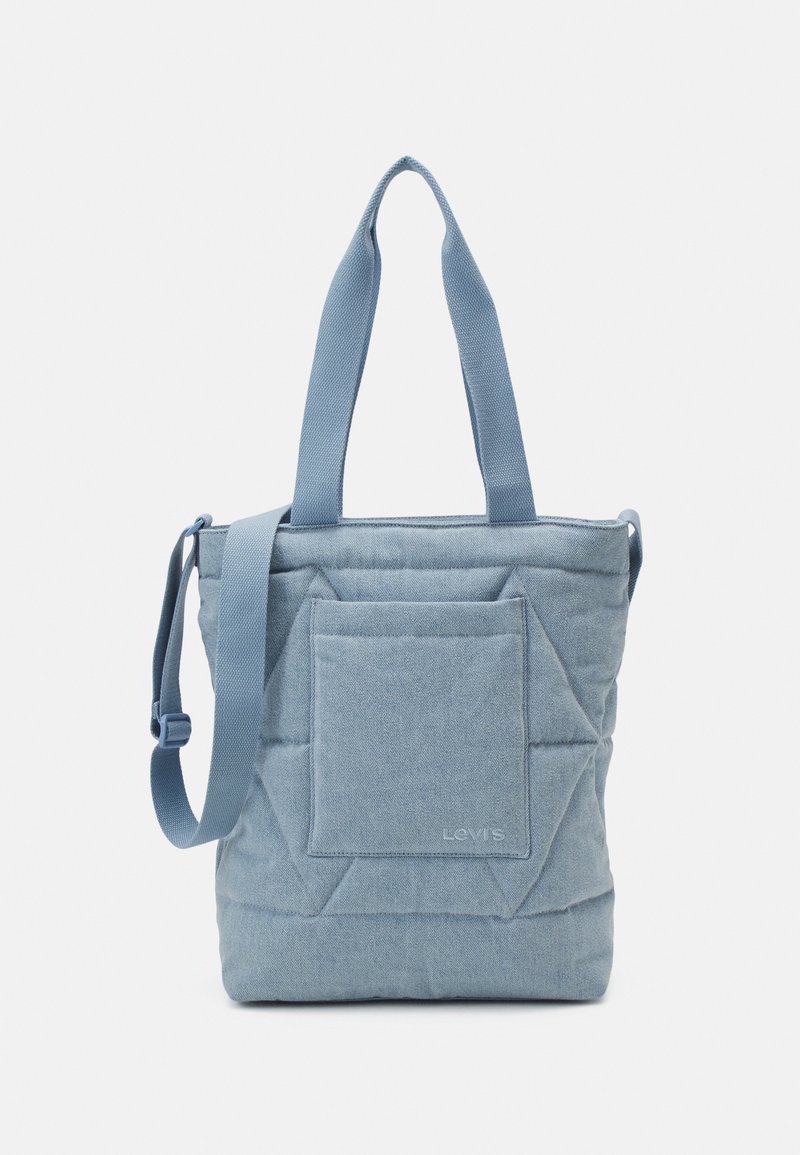 Sac cabas matelassé bleu clair avec deux poignées supérieures et une bandoulière réglable. Comprend une poche avant et un détail de logo subtil.