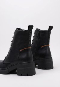 Botas negras de imitación cuero hasta el tobillo con un tacón grueso, cordones en la parte frontal, cremallera lateral y detalle de costura en naranja contrastante.
