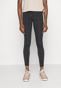 Svarta leggings med en mjuk, elastisk textur och vertikala sömmar, kombinerat med en beiges kortärmad topp och ljusrosa sneakers.