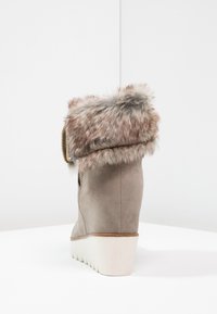 Vinkelt ankle boots i taupe ruskind med en faux fur krave, prydet med en sidelukning og en hvid gummisål med struktureret mønster.