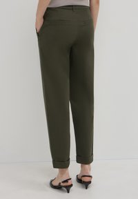 Pantaloni verde oliva con taglio dritto, dotati di orlo a costine, due tasche posteriori e una texture liscia. Indossati con sandali neri con tacco.