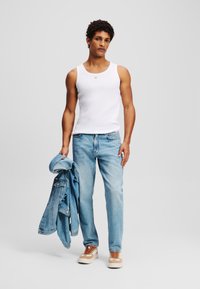 Balti medvilnės marškiniai be rankovių, šviesiai mėlyni džinsai ir šviesiai mėlynas džinsinis švarkas laikomas rankoje. Rudos ir baltos sportbačiai su nėriniais.