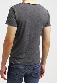 Grå kortærmet t-shirt, lavet af bomuldsmateriale, tætsiddende design, rund halsudskæring, synlige syninger, parret med blå denim jeans, set bagfra.